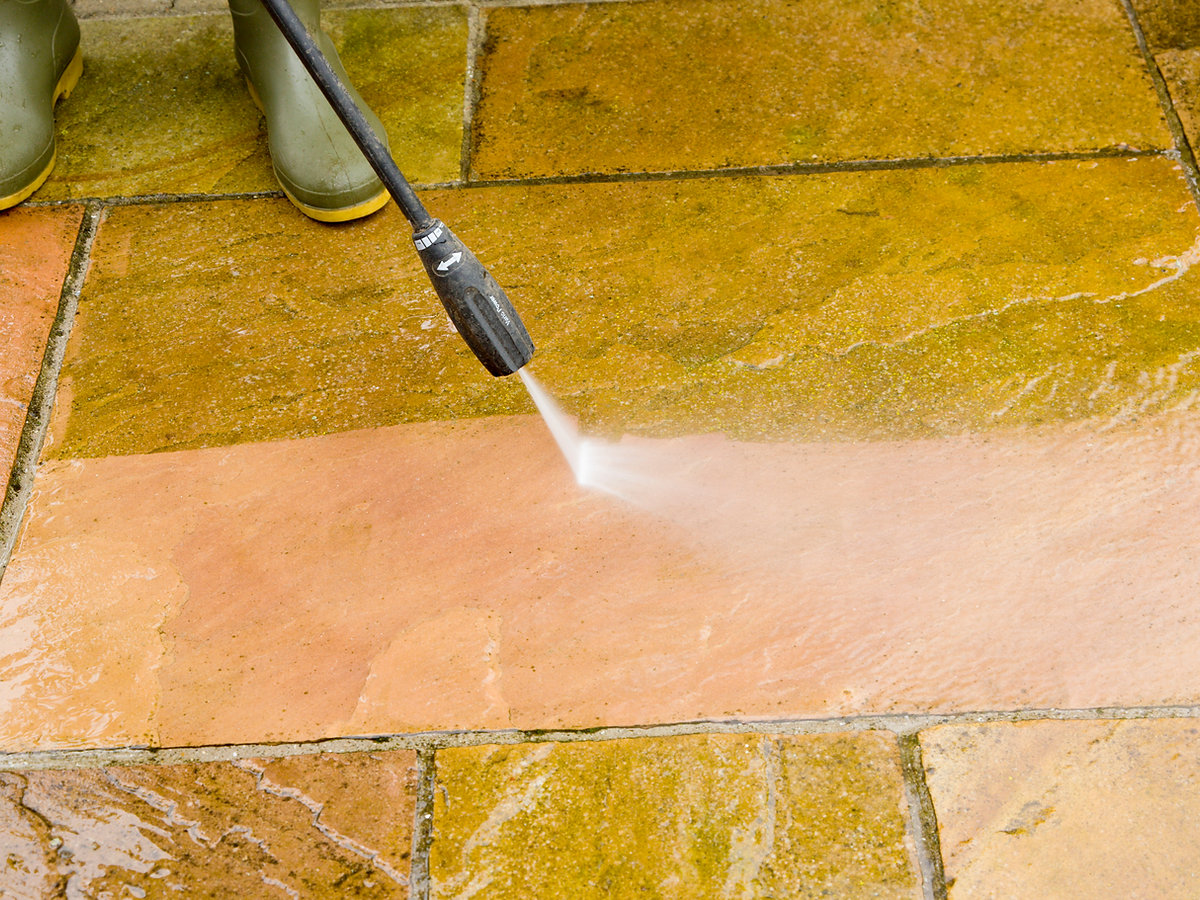 Man wearing wellingtons jet washing Indian Sandstone patio
